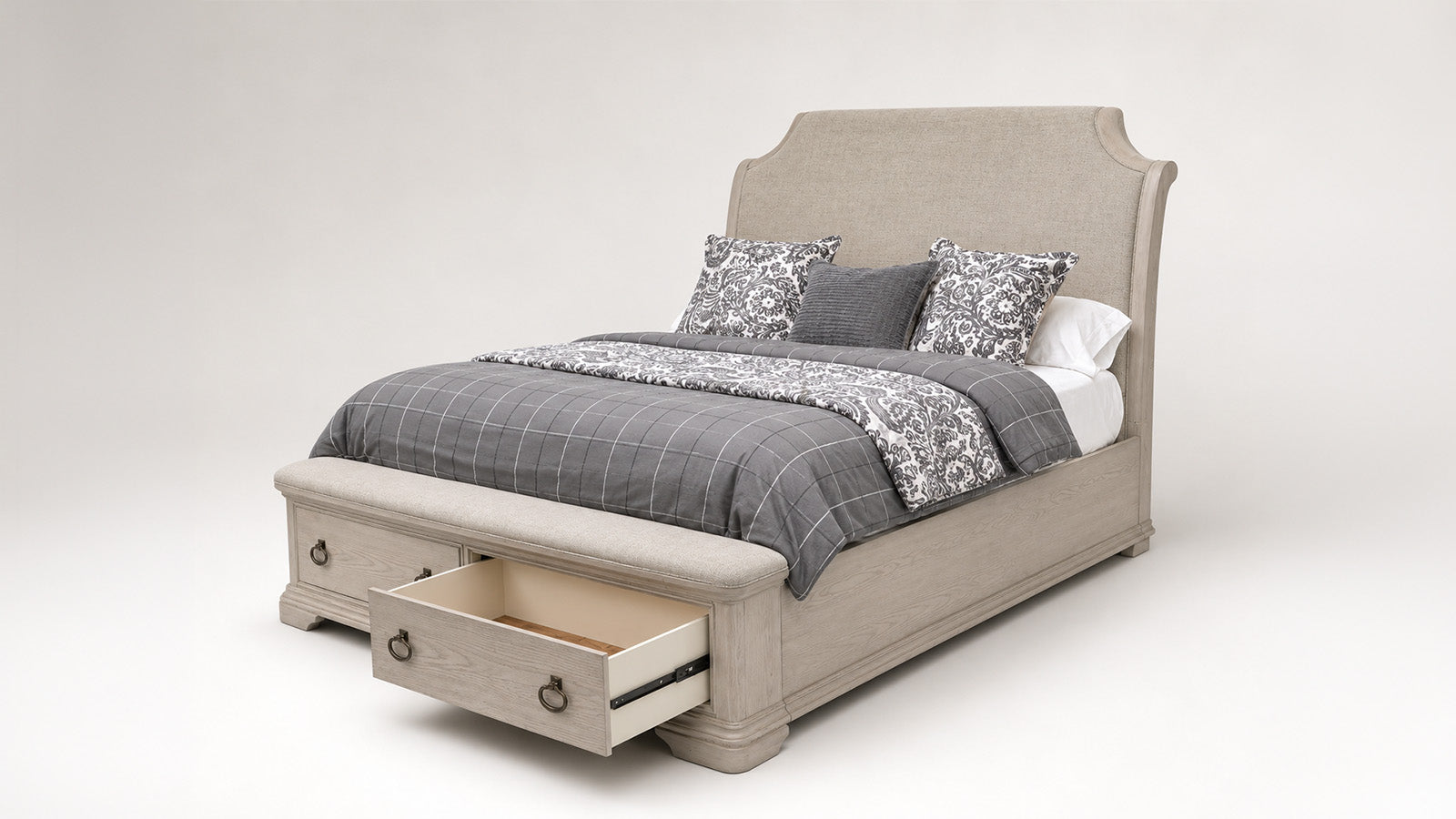 A light beige upholstered bed frame with a tall curved headboard and built-in storage drawers at the foot, shown with gray plaid bedding and patterned pillows on a neutral studio background.