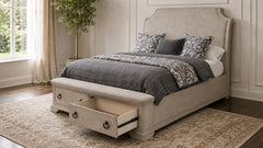 A light beige upholstered bed frame with a tall curved headboard and built-in storage drawers at the foot, shown in a styled bedroom with gray bedding, patterned pillows, and an open drawer pulled out.