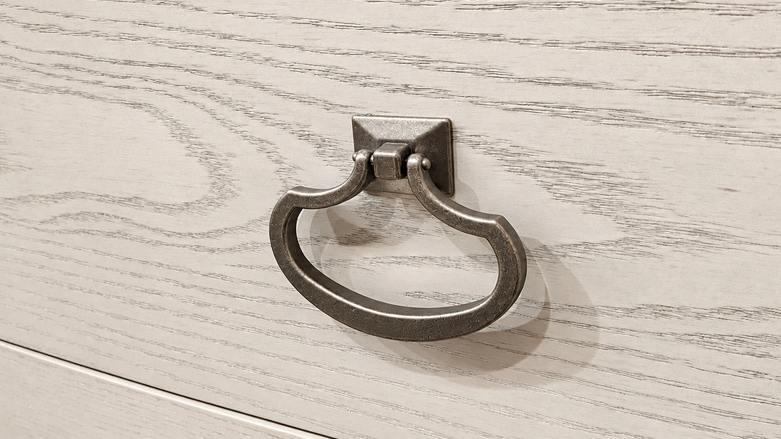 A dark metal pull ring cabinet knob mounted on a light-colored wood drawer front.