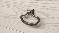 A dark metal pull ring cabinet knob mounted on a light-colored wood drawer front.