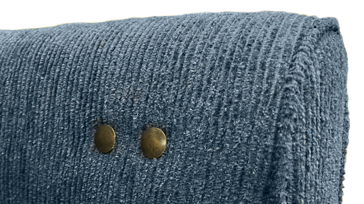 Close-up of a textured blue upholstered furniture corner with two brass nailhead accents on a white background.