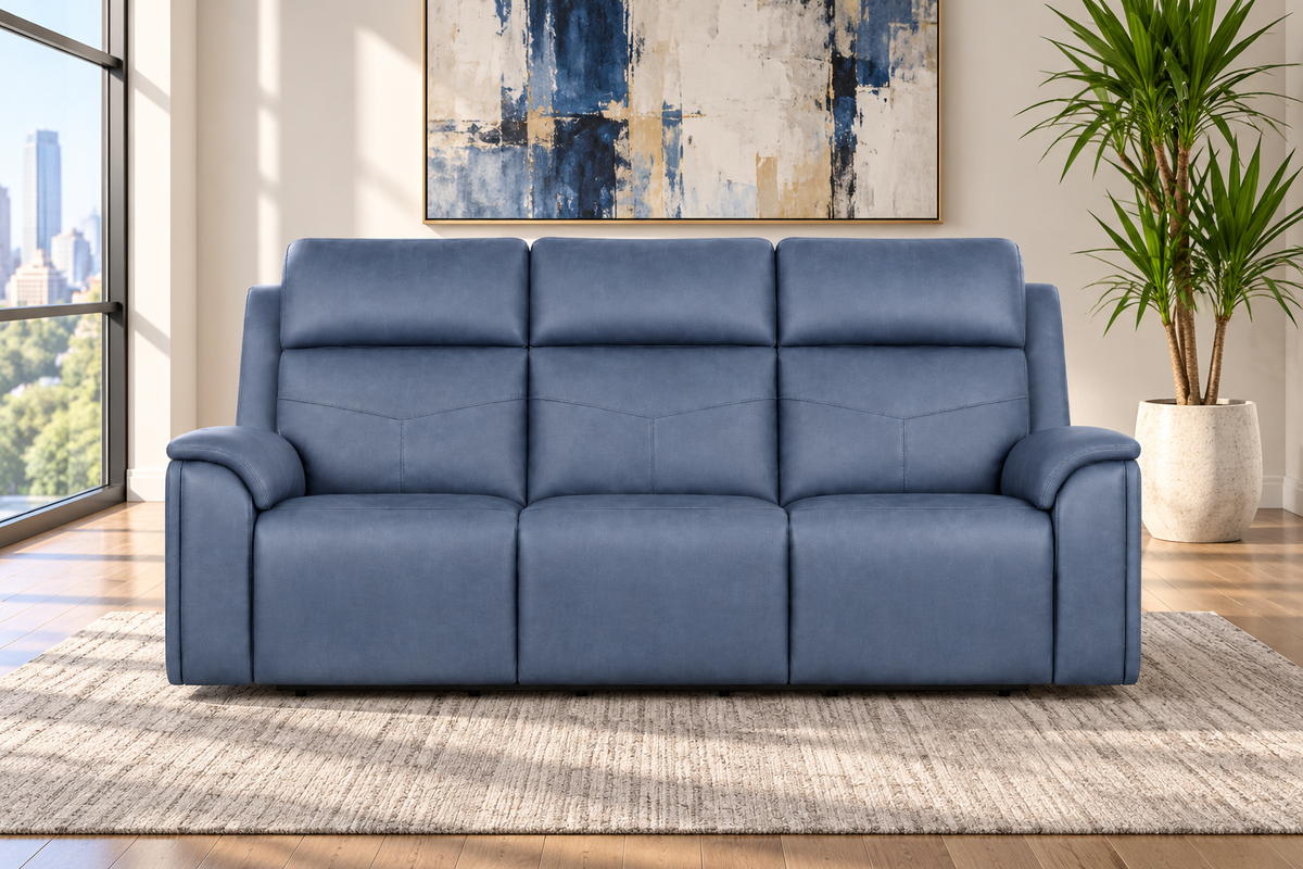 A three-seat blue leather reclining sofa positioned on a textured beige rug in a modern living room setting with a window, city view, and a potted plant.