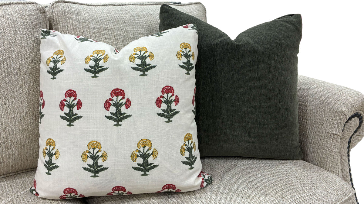 Two decorative throw pillows on a light gray upholstered sofa. The front pillow is off-white with a repeating block-print style floral pattern in red, yellow, and green.
