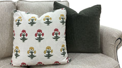 Two decorative throw pillows on a light gray upholstered sofa. The front pillow is off-white with a repeating block-print style floral pattern in red, yellow, and green.
