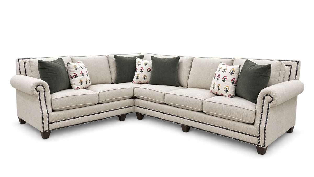 An L-shaped sectional sofa upholstered in light beige fabric with dark green and floral accent pillows, shown on a plain white background.