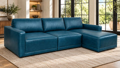 A modern sectional sofa with a right-facing chaise lounge in deep teal blue leather, styled on a beige woven rug in a bright living room.