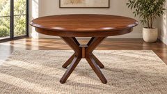 A round wooden dining table with a dark brown finish and a central X-shaped pedestal base, shown in a bright room on a textured rug.