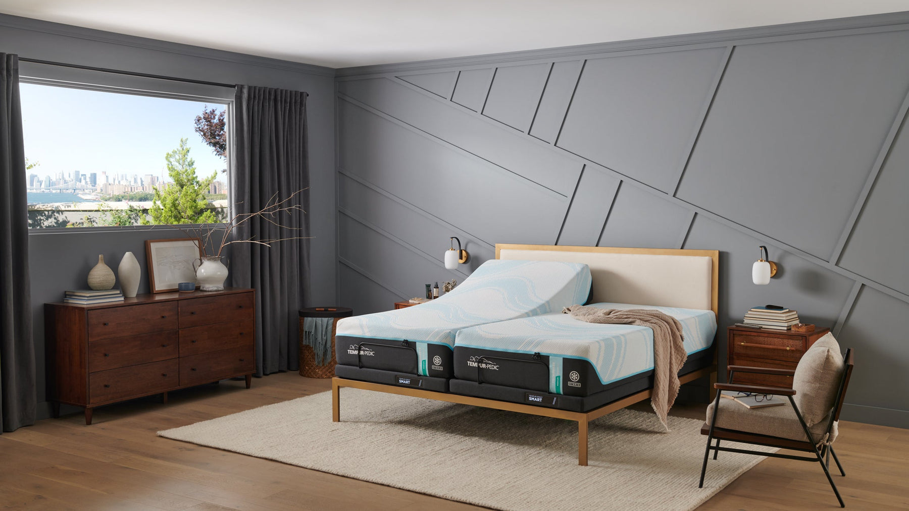 Cama con colchón híbrido medio Breeze sobre un somier de madera en un dormitorio moderno con grandes ventanas y paredes grises.
