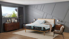 Cama con colchón híbrido medio Breeze sobre un somier de madera en un dormitorio moderno con grandes ventanas y paredes grises.