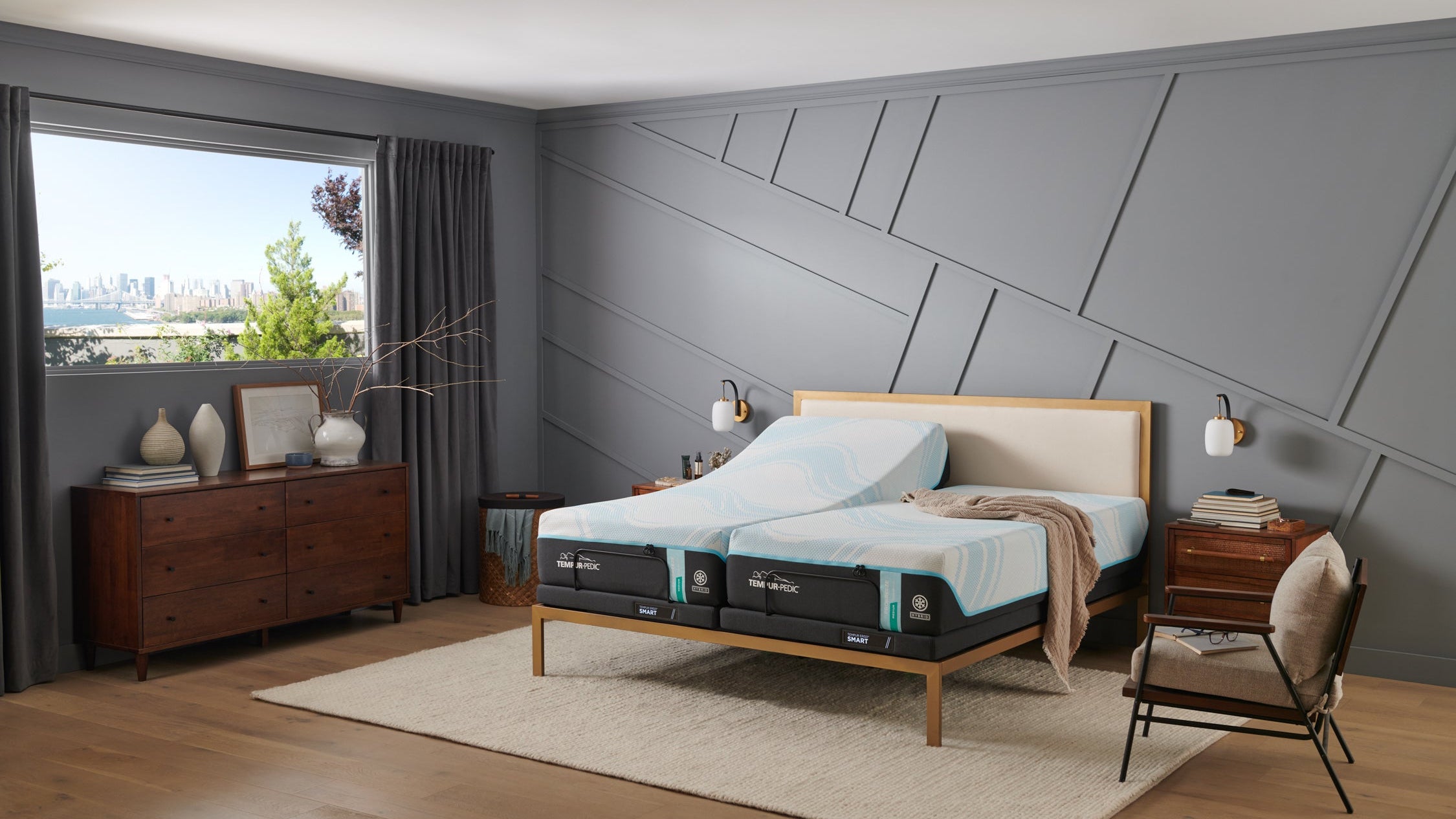 Cama con colchón híbrido medio Breeze sobre un somier de madera en un dormitorio moderno con grandes ventanas y paredes grises.