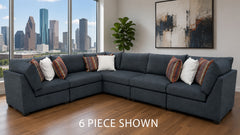 A 6-piece sectional sofa in a dark slate blue-gray fabric, styled with white and striped accent pillows in a modern living room with a city skyline view.
