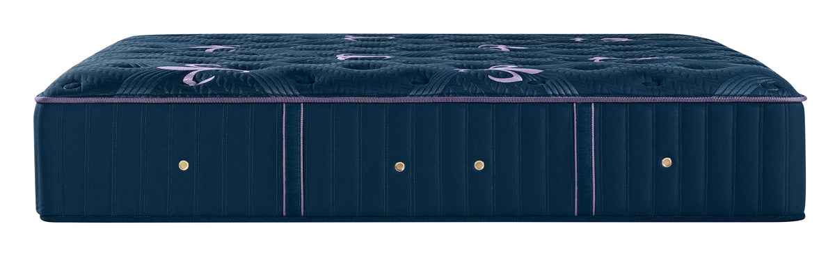 A luxury tufted mattress shown from a side profile view, featuring deep navy blue upholstery with purple piping accents and gold button details.