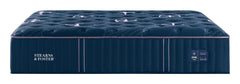 A Stearns & Foster mattress shown from a three-quarter angle against a solid white background. The mattress features a deep navy blue tufted top with subtle pinkish-purple accents, a matching navy blue side panel with the brand name in white, and thin vertical pink piping along the edge.