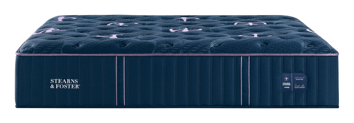 A Stearns & Foster mattress shown from a three-quarter angle against a solid white background. The mattress features a deep navy blue tufted top with subtle pinkish-purple accents, a matching navy blue side panel with the brand name in white, and thin vertical pink piping along the edge.
