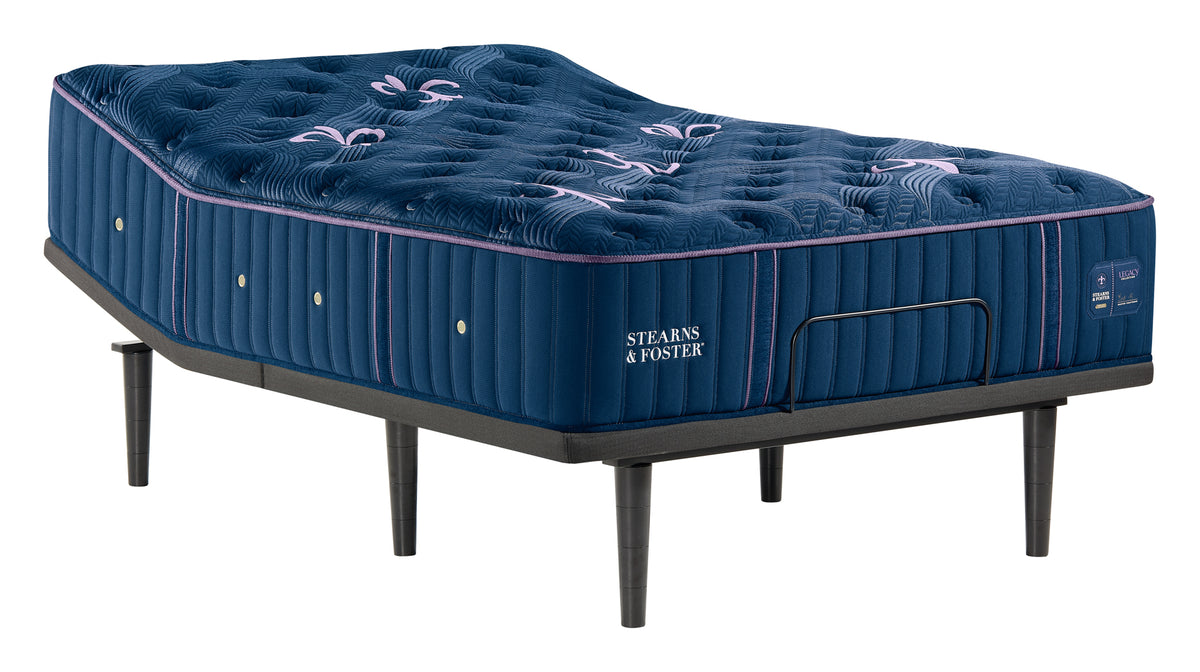 Steavns & Foster mattress on a black metal bed frame, shown against a solid white background. The mattress is deep navy blue with tufted floral detailing on top and pink piping along the edges.