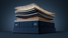 A luxury mattress stack display featuring a dark navy blue mattress on a matching base, with layered mattress toppers in cream, beige, and navy floating above it against a dark blue studio background.