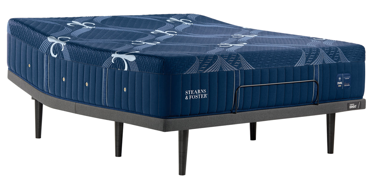 A Stearns & Foster mattress on a black metal bed frame, shown from a three-quarters angle against a solid white background.