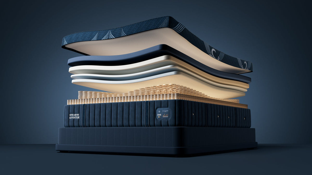 A luxury mattress stack displayed on a dark studio background, showing multiple layers of navy, cream, and beige materials with a glowing interior.