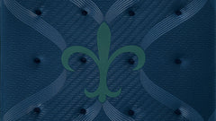 A square tufted mattress topper or mattress top in dark navy blue, featuring a subtle textured herringbone pattern, tufted button details, and a central green fleur-de-lis logo.
