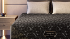 Black hybrid mattress on a bed with beige pillows in a modern bedroom setting.