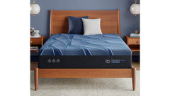 Bed with blue mattress topper and wooden headboard against a blue wall.