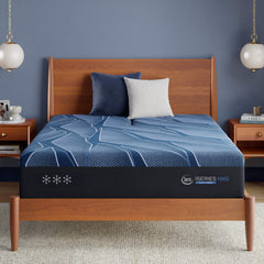 Colchón azul con el logotipo de una marca sobre un somier de madera contra una pared azul.