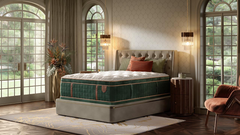 A luxury mattress on a matching upholstered bed frame in a beautifully styled bedroom with tall arched windows, warm lighting, and a plush armchair.
