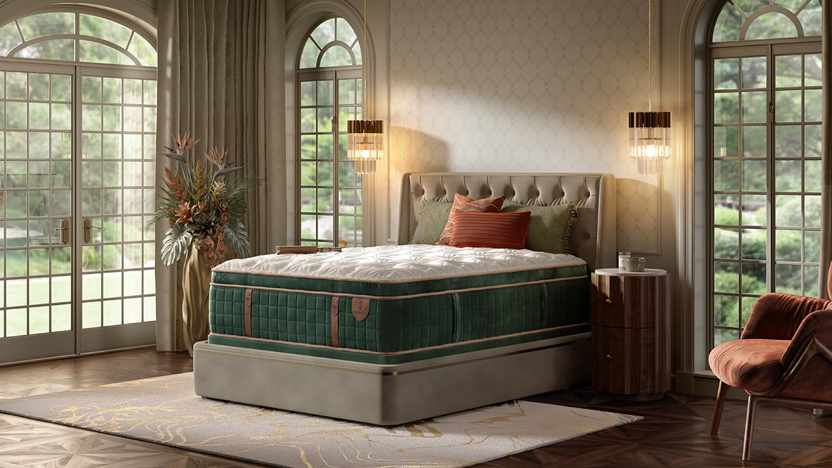 A luxury mattress on a matching upholstered bed frame in a beautifully styled bedroom with tall arched windows, warm lighting, and a plush armchair.