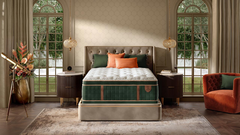 A luxury mattress on an upholstered bed frame in a beautifully styled bedroom. The mattress features a white quilted top and a green tufted side panel with gold trim.