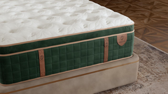 A close-up of a mattress on a bed frame, showing a white tufted top with a quilted green side panel and tan leather-like straps. The brand name 'Majestic' is visible on the side label.