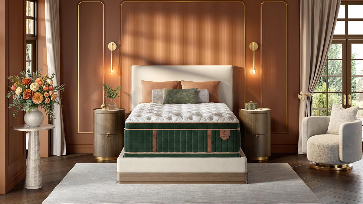 A luxury bed with a tufted white mattress and a dark green velvet side panel, styled in a modern, warm brown bedroom with gold wall accents, side tables, and a matching armchair.