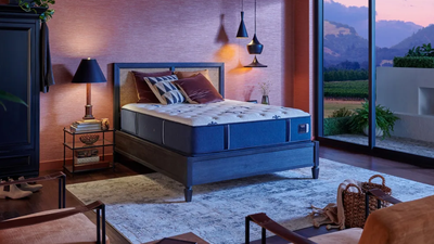 A queen-sized Stearns & Foster Studio Medium Tight Top Mattress on a bed frame, displayed in a cozy bedroom setting with nightstands and window in the background.