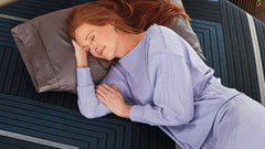 Woman sleeping on a bed with a blue pillow and purple pajamas.