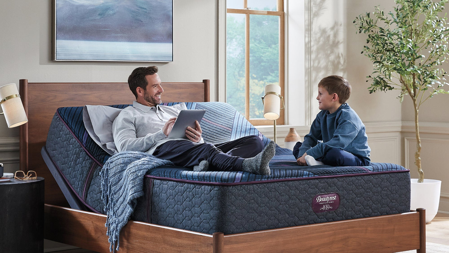 Two people on a adjustable bed in a room with a large window and plant.
