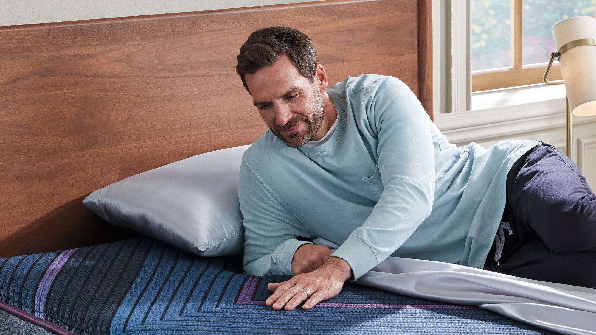 Man lying on a blue mattress with a wooden headboard in a bedroom.