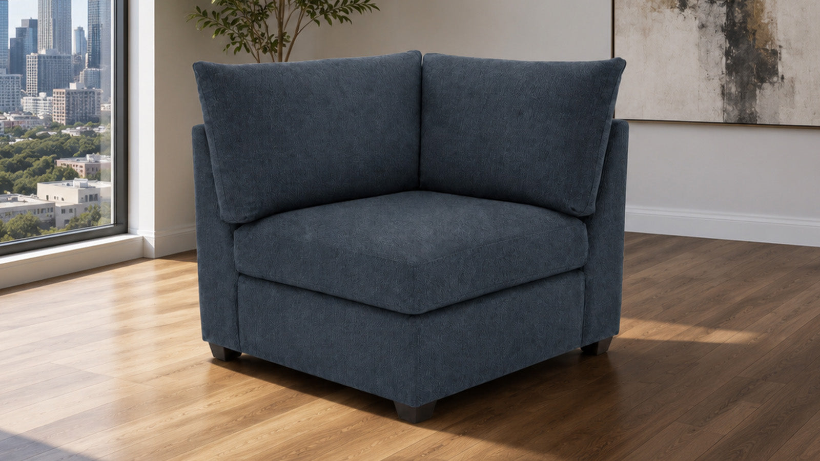 A modern two-seat armchair upholstered in textured slate blue fabric, positioned on a light wood floor in a contemporary room with a city view window and abstract wall art.