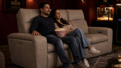 Man and woman sitting on a couch with popcorn, watching a movie in a theater setting.