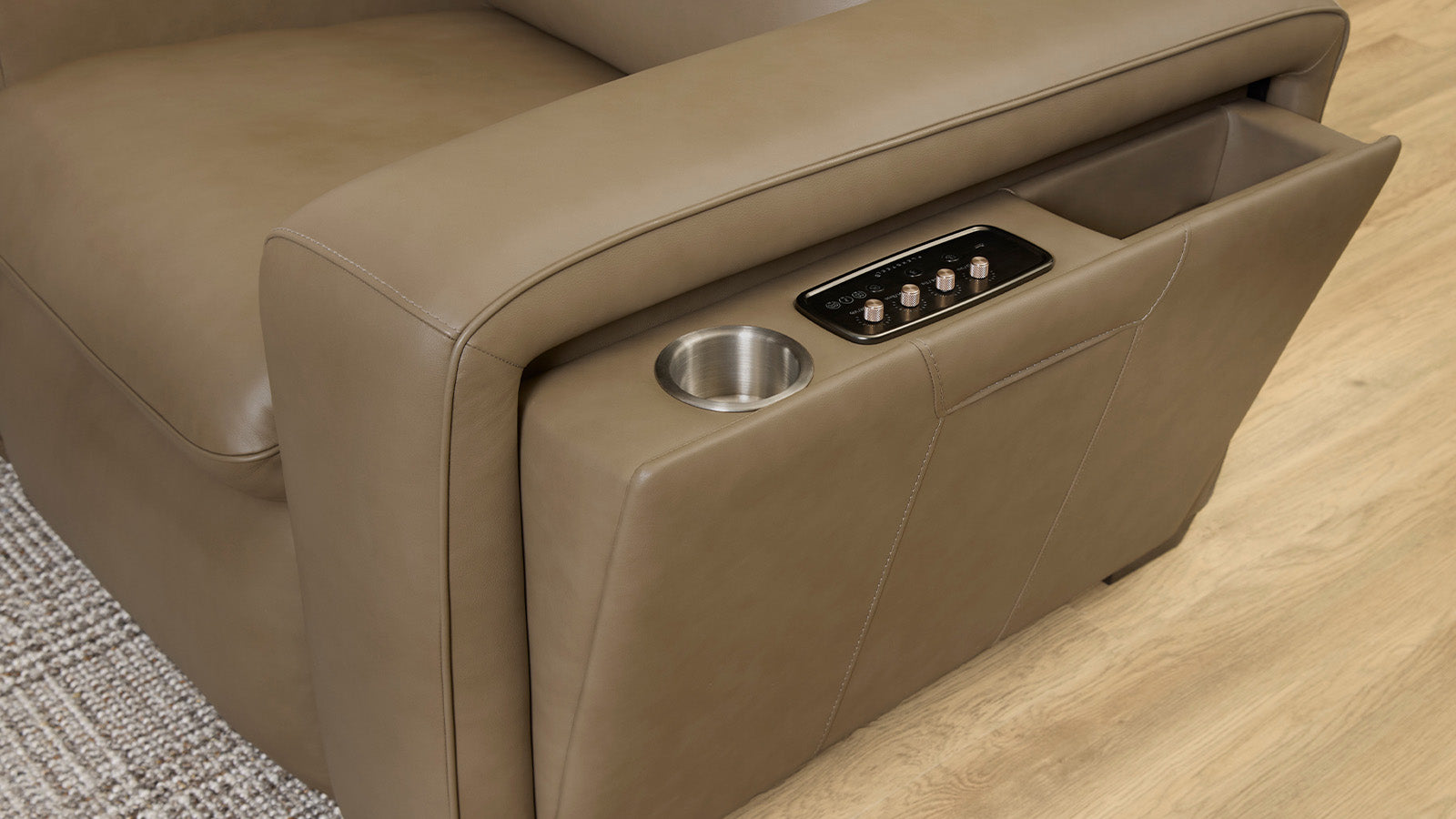 Beige leather sofa with cup holder and storage compartment on a wooden floor.