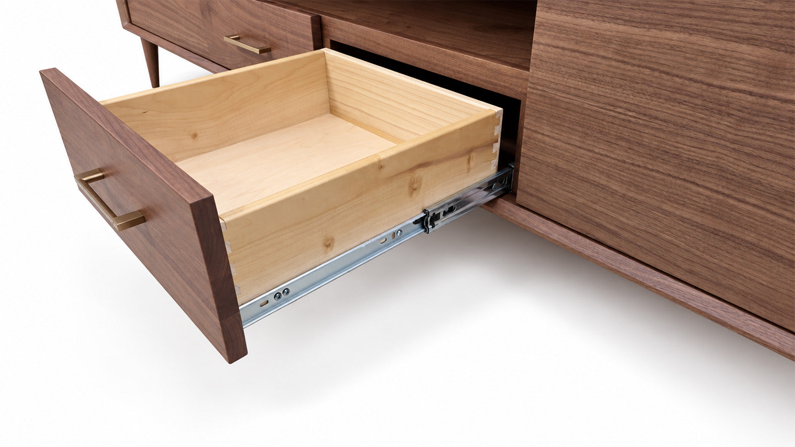 A close-up of a wooden cabinet with one drawer pulled open, showing a light natural wood drawer interior and metal drawer slides against a white background.