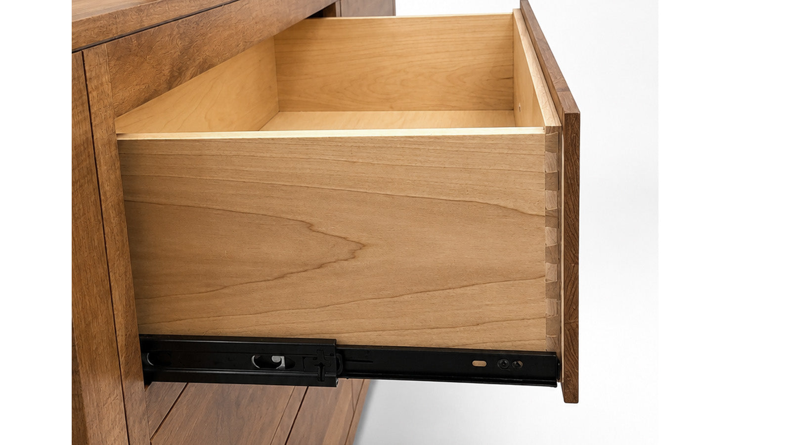 Close-up of a wooden drawer pulled open, showing the interior wood grain and a black metal drawer slide mechanism at the bottom, set against a white background.
