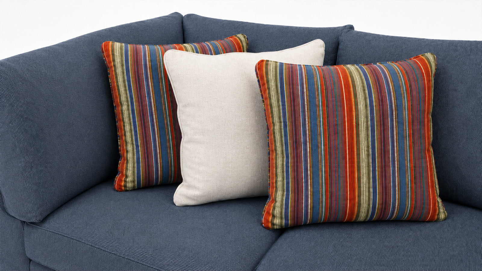 Three decorative throw pillows on a blue fabric sofa: two striped pillows in red, orange, blue, green, and beige tones, and one plain off-white pillow.