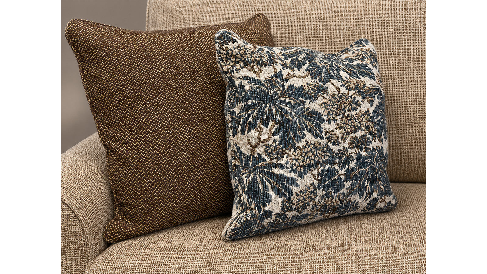 Two pillows, one brown and one with a floral pattern, on a beige couch.