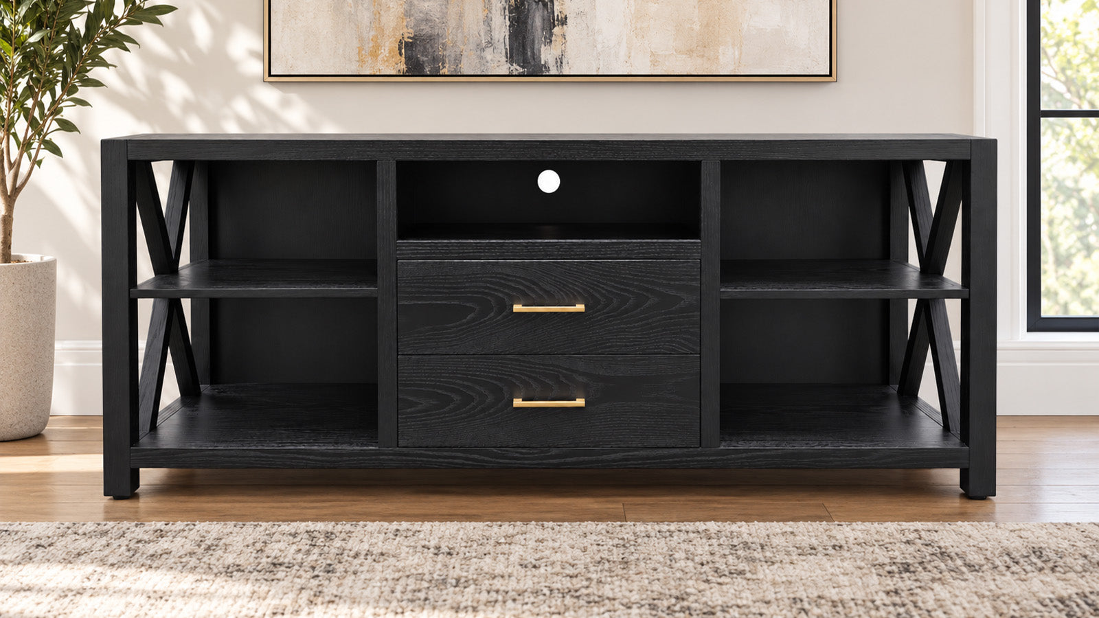 A black wood media console with two drawers featuring gold handles, open side shelves, and X-shaped metal support legs, shown in a styled living room setting.