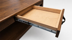 Close-up of a wooden desk drawer partially pulled out, showing a light natural wood drawer interior and metal drawer slides against a white background.