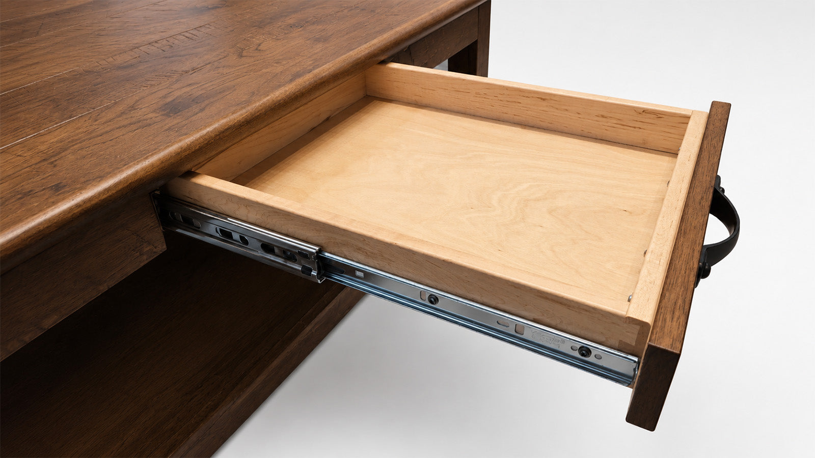 Close-up of a wooden desk drawer partially pulled out, showing a light natural wood drawer interior and metal drawer slides against a white background.