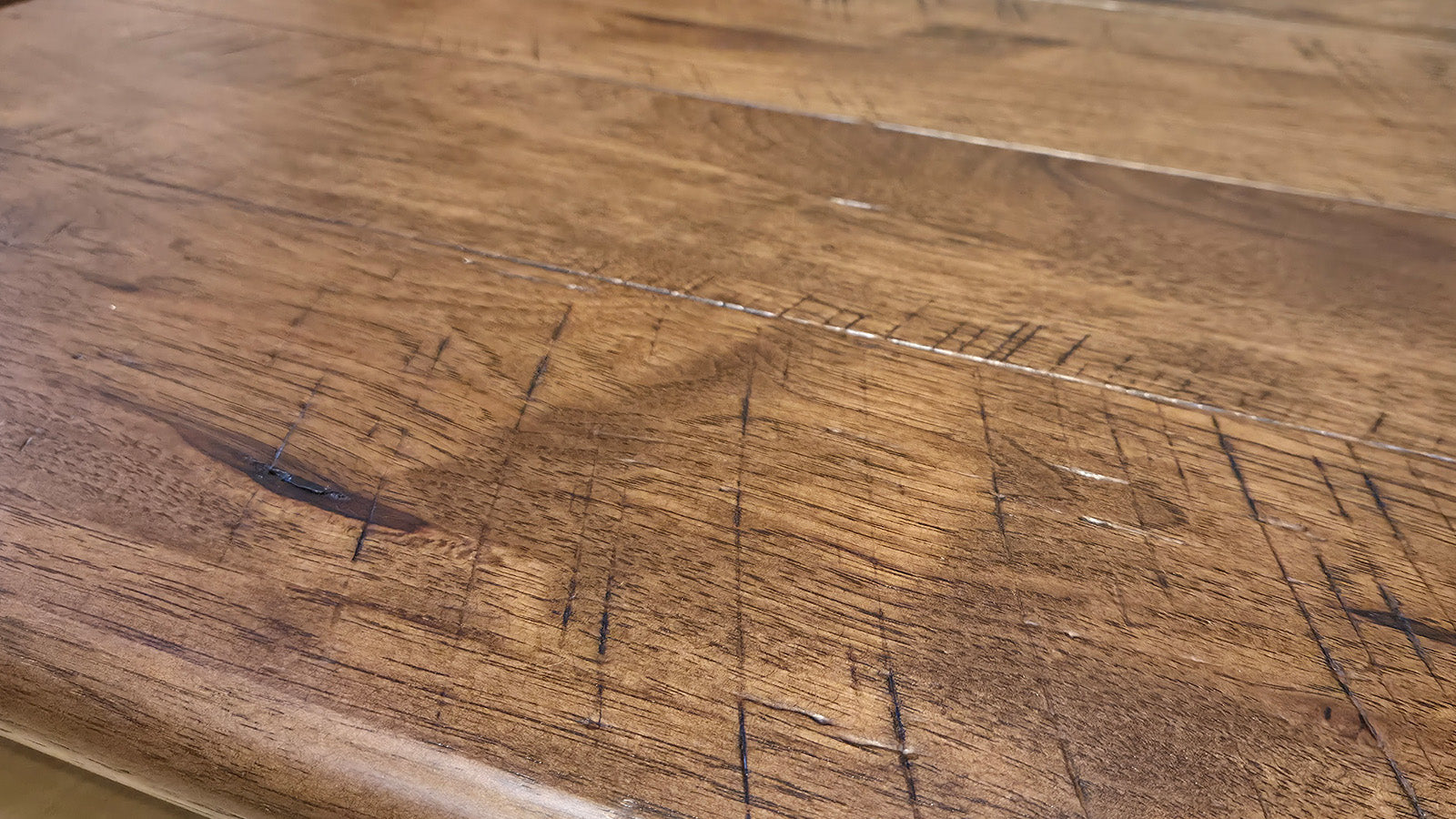 Close-up of a medium brown wooden surface showing natural wood grain, knots, and visible scratches or wear marks.