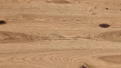 A close-up of a natural wood surface with visible grain, knots, and warm tan-brown tones.
